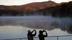 Pasangan mengambil foto saat matahari terbit di Price Lake sepanjang Blue Ridge Parkway dekat Blowing Rock, North California, saat musim gugur tiba, pada 19 Oktober 2021. (AP Photo/Gerry Broome)
