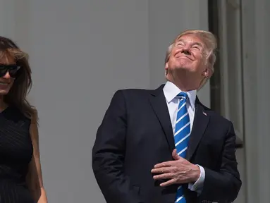 Presiden AS Donald Trump bersama Ibu Negara, Melania Trump menyaksikan  gerhana matahari dari balkon Gedung Putih di Washington, Senin (21/8). Trump tertangkap kamera menyaksikan fenonema langka tersebut tanpa kacamata pelindung. (NICHOLAS KAMM/AFP)