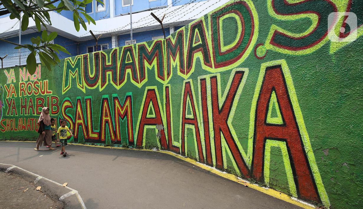 Warga berjalan di depan mural bernuansa Islami di Gang Pelangi, kawasan Kalibata, Jakarta, Jumat (23/4/2021). Mural bernuansa Islami tersebut dibuat untuk menghiasi dan meramaikan pintu masuk gang sekaligus mengingatkan masyarakat untuk selalu beribadah dan bershalawat (Liputan6.com/Herman Zakharia)