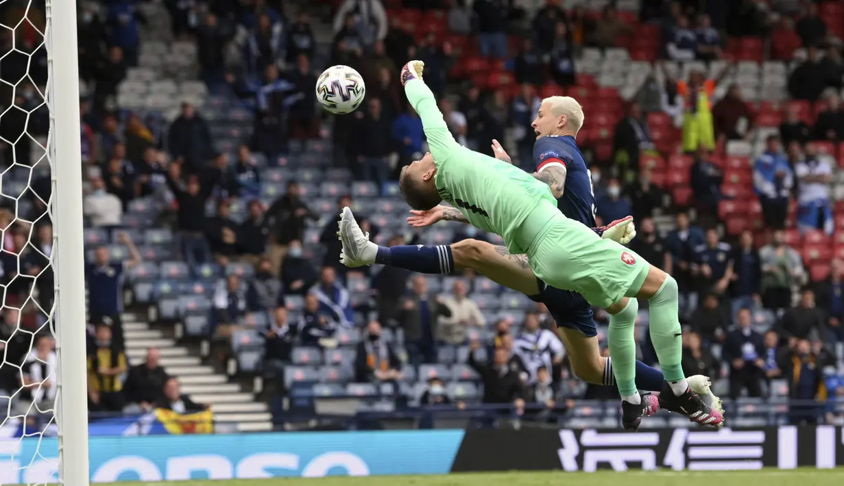 Kiper Republik Ceko, Tomas Vaclik berusaha menepis bola dari sundulan pemain Skotlandia, Lyndon Dykes pada pertandingan grup D Euro 2020 di stadion Hampden Park, Glasgow, Senin (14/6/2021). Dengan kemenangan ini, Ceko menggeser Inggris dari puncak klasemen sementara. (Stu Forster, Pool via AP)