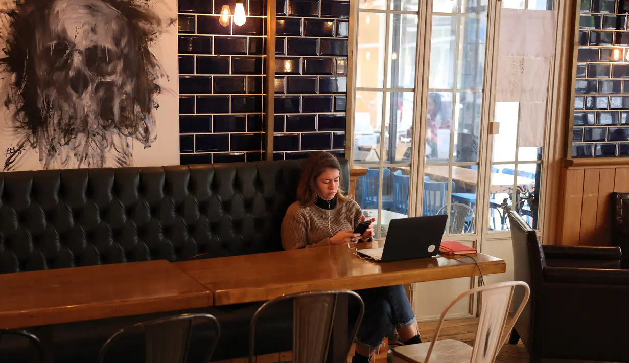 Seorang perempuan duduk dengan laptopnya di sebuah kafe di Beirut pada 14 Januari 2022. Kafe-kafe Beirut sekarang berfungsi sebagai tempat kerja pengganti bagi orang-orang yang bergulat dengan kekurangan listrik dan pemutusan internet yang berasal dari krisis ekonomi. (JOSEPH EID / AFP)