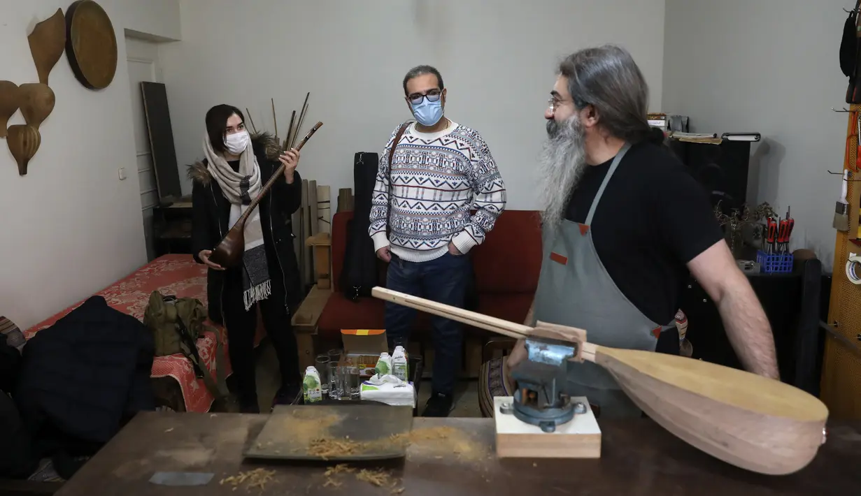 Luthier Ali Akbar Soleimani (kanan) berbicara dengan pelanggannya di bengkel kerjanya di Teheran pada 28 Januari 2021. Selain sumber penghasilan, pembuatan beragam alat musik tradisional itu juga menjadi salah satu upaya Soleimani untuk melestarikannya. (AP Photo/Vahid Salemi)
