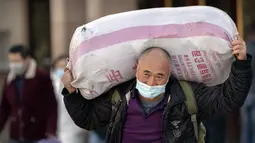Seorang pelancong yang mengenakan masker untuk melindungi dari penyebaran virus corona membawa kopernya saat dia berjalan keluar dari pintu keluar di Stasiun Kereta Api Beijing di Beijing, Kamis (28/1/2021).  (AP Photo/Mark Schiefelbein)