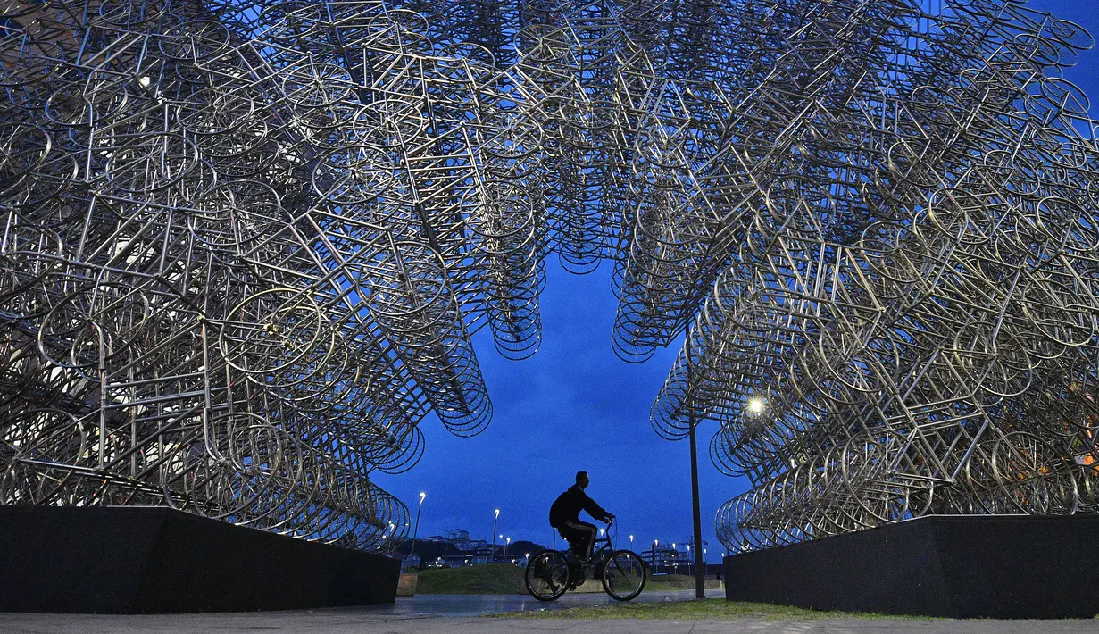 Seorang pria mengendarai sepeda melewati instalasi seni seniman China Ai Weiwei yang berjudul 'Forever Cycles' di Rio de Janeiro, Brasil, Senin (19/8/2019). Instalasi Ai Weiwei ini akan dibuka pada 21 Agustus 2019. (CARL DE SOUZA/AFP)