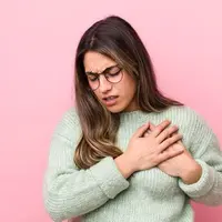 Seorang perempuan berbaju hijau tampak kesakitan dan memegang bagian dadanya (Foto Dok: Freepik/kues1).