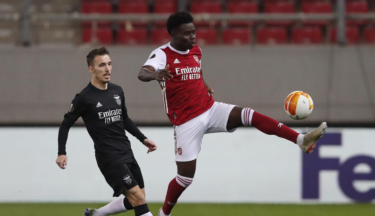 Striker Arsenal, Bukayo Saka (kanan) menguasai bola dibayangi bek Benfica, Alex Grimaldo dalam laga leg kedua babak 32 Besar Liga Europa 2020/21 di Georgios Karaiskakis Stadium, Kamis (25/2/2021). Arsenal menang 3-2 atas Benfica. (AP/Thanassis Stavrakis)