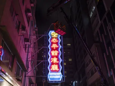 Pekerja menghapus tanda neon yang digantung di gedung restoran Tai Ping Koon sejak 1964 di Hong Kong, Minggu, 6 Agustus 2023. Dulunya ada di mana-mana di jalan-jalan Hong Kong, tanda neon ikonik kota itu menghilang karena pengetatan peraturan pemerintah. (AP Photo/Louise Delmotte)