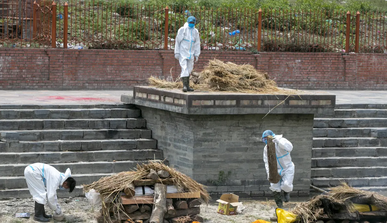 Pria Nepal dengan pakaian pelindung mengatur tumpukan kayu pemakaman untuk mengkremasi jenazah korban COVID-19 di dekat kuil Pashupatinath di Kathmandu, Nepal (3/5/2021). (AP Photo/Niranjan Shrestha)