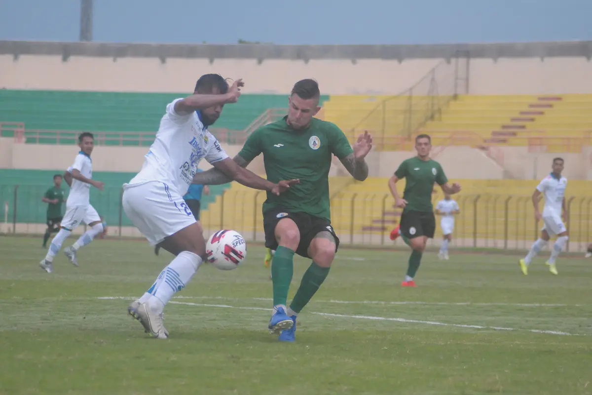 Bek PSS Sleman, Aaron Evans (hijau) berduel dengan striker Persib Bandung, Zulham Zamrun