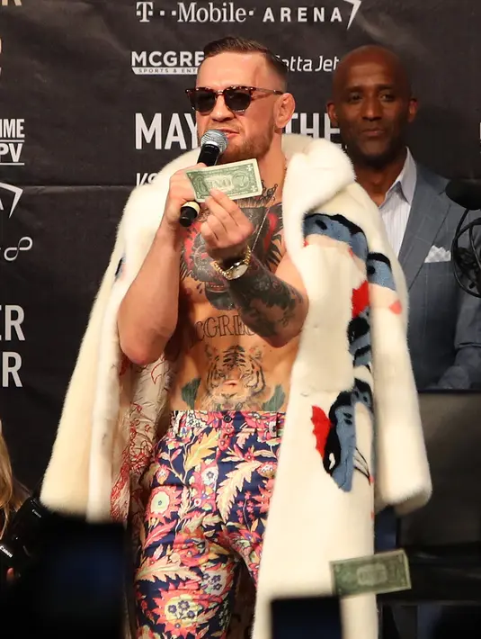 Juara mixed martial arts Conor McGregor memegang selembar uang yang dilemparkan petinju Floyd Mayweather Jr saat konferensi pers tur dunia jelang pertandingannya di Barclays Center, Brooklyn, (13/7). (Mike Lawrie/Getty Images/AFP)
