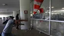 Anggota polisi memecahkan jendela saat mencoba masuk ke Gedung Kongres Nasional Brasil selama unjuk rasa, Brasilia (18/4). RUU yang diusulkan oleh Presiden Brasil Michel Temer ini menetapkan usia pensiun polisi adalah 65 tahun. (AP Photo / Eraldo Peres)