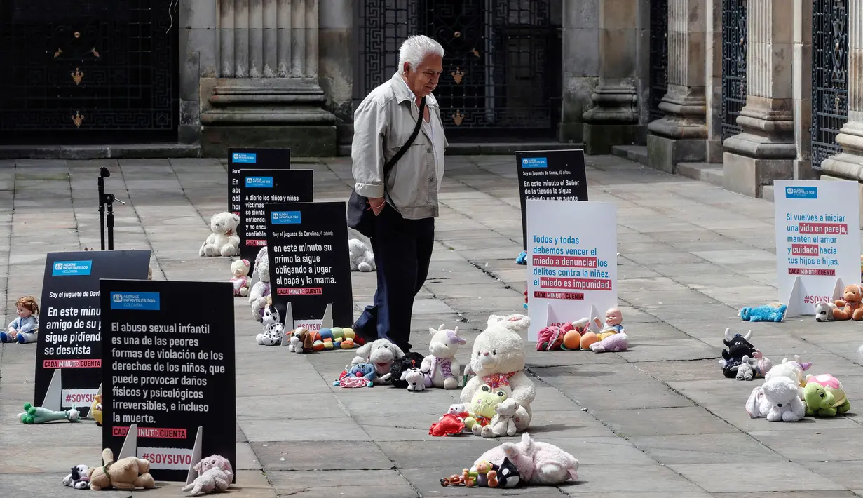 Seorang pria melewati boneka mainan yang diletakkan di halaman gedung Kongres Kolombia saat aksi protes di Bogota, Selasa (20/11). Protes ini bertujuan untuk mendorong pengaduan kasus pelecehan anak di hadapan pihak berwenang Kolombia (DANIEL MUNOZ/AFP)