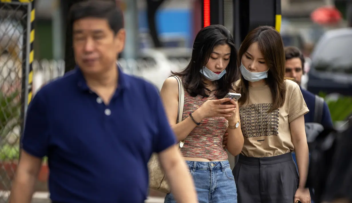 Dua perempuan melihat smartphone saat mereka berdiri di sudut jalan di Beijing, Rabu (6/7/2022). Warga beberapa bagian Shanghai dan Beijing telah diperintahkan untuk menjalani tes massal COVID-19 lebih lanjut menyusul ditemukannya kasus baru di dua kota, sementara pembatasan tambahan tetap berlaku di Hong Kong, Makau, dan kota-kota lain. (AP Photo/Mark Schiefelbein)