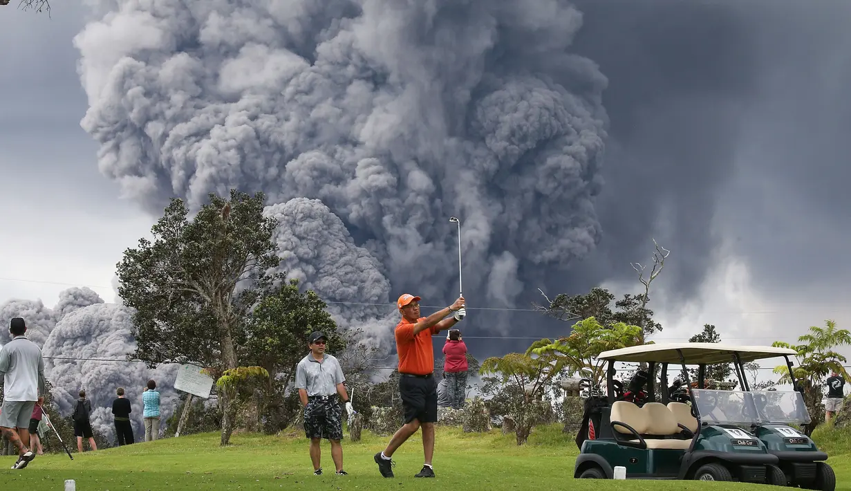 Orang-orang bermain golf saat kepulan asap abu vulkanik berembus dari puncak gunung Kiluaea di Big Island Hawaii (15/5). Letusan gunung tersebut tidak membuat sejumlah orang khawatir bahkan masih ada yang bermain golf. (AFP Photo/Mario Tama)