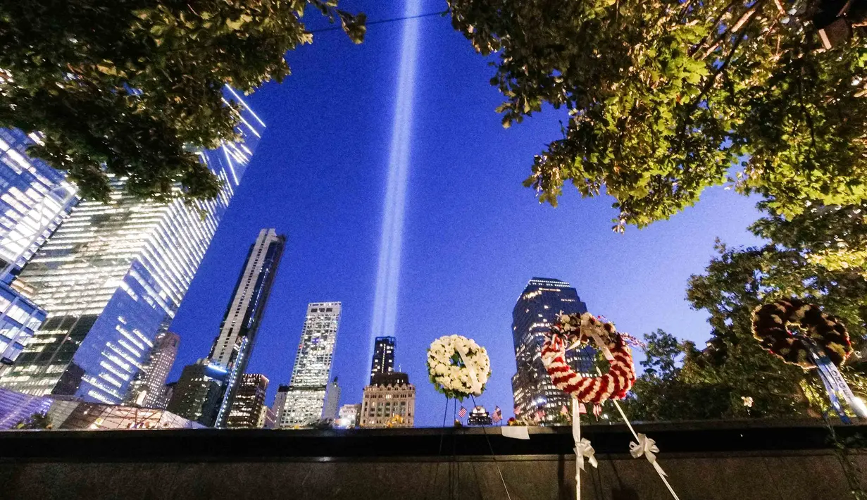 Karangan bunga peringatan ditinggalkan di 9/11 Memorial & Museum saat Tribute in Light tahunan memproyeksikan dua pilar cahaya ke langit malam di New York City (10/9/2021). Cahaya kembar itu untuk peringati serangan 11 September 20 tahun silam. (AFP/Roberto Schmidt)