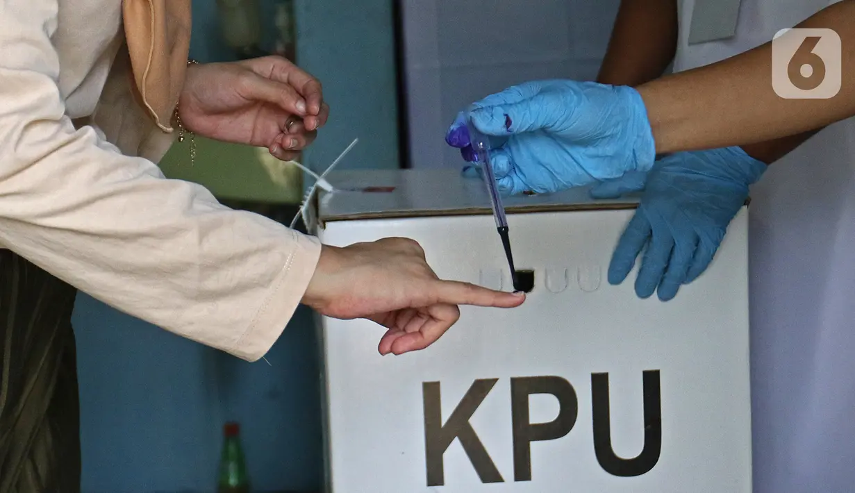 Petugas menandai jari warga dengan tinta usai mencoblos saat Pilkada Depok di TPS 56, Mekarjaya, Depok, Rabu (9/12/2020). TPS 56 menggunakan tema kesehatan untuk menarik warga menggunakan hak pilih dan mengingatkan protokol kesehatan di masa Pandemi COVID-19. (Liputan6.com/Herman Zakharia)
