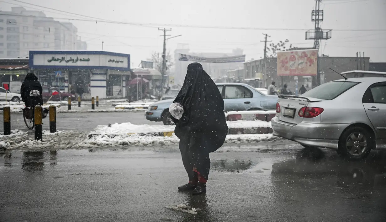 Seorang wanita mengenakan burqa memohon di sepanjang jalan saat hujan salju di Kabul (4/1/2022). Sedikitnya tujuh warga Afghanistan tewas dan 26 lainnya cedera dalam beberapa kecelakaan lalu lintas. (AFP/Mohd Rasfan)