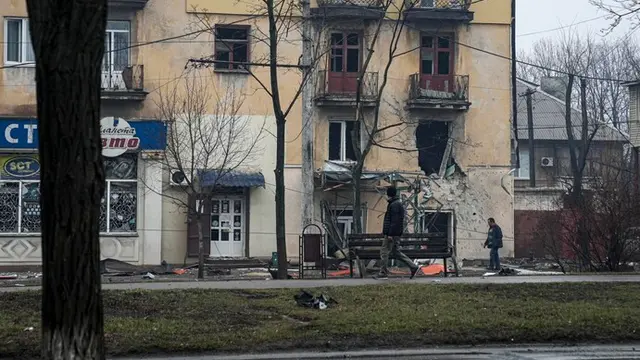 Seorang pria berjalan melewati sebuah gedung apartemen pada 2 Maret yang dirusak oleh penembakan Rusia di Mariupol, Ukraina. (Evgeniy Maloletka/AP)