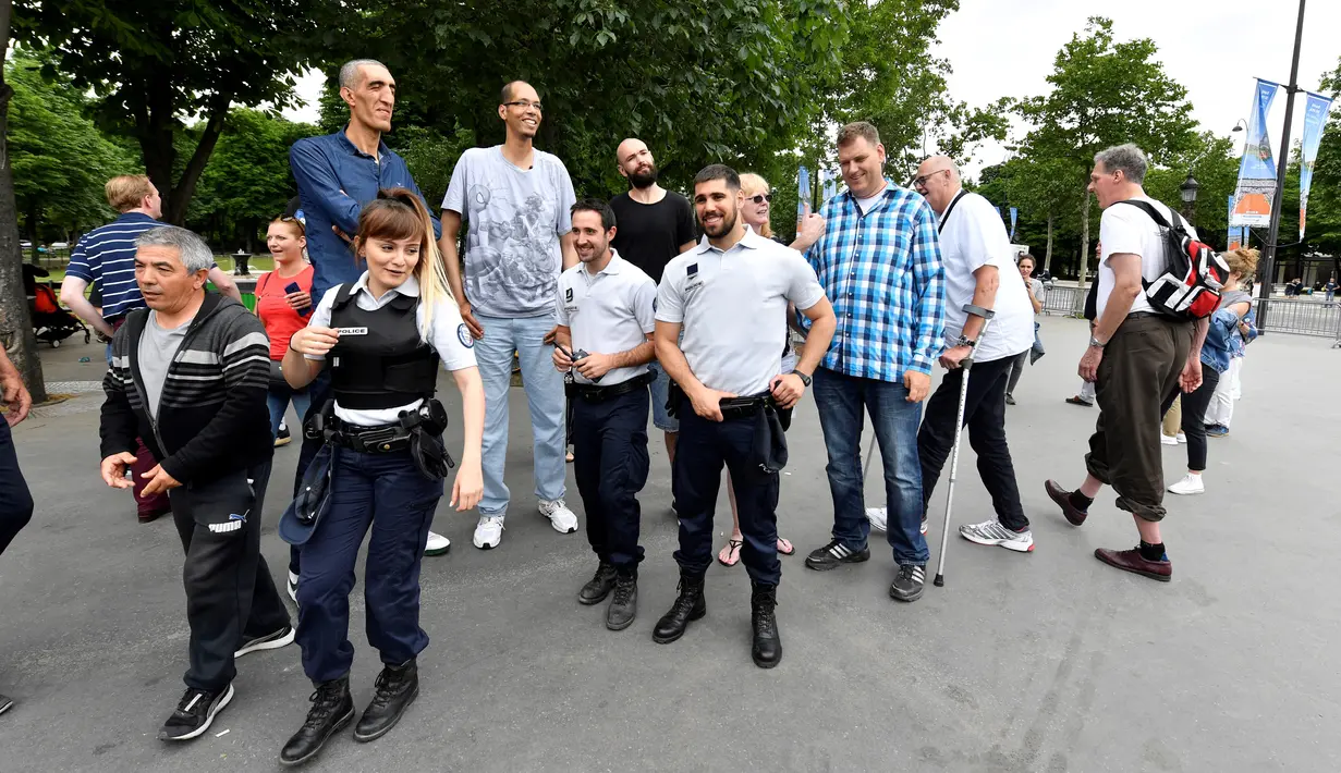 Arshavir Grigoryan dari Armenia (2,33 meter) dan Brahim Takioullah dari Prancis (2,46) berpose dengan aparat kepolisian di Champs-Elysees Avenue, Paris, 1 Juni 2018. Belasan pria tertinggi di dunia bertemu pada akhir pekan di Paris. (AFP/GERARD JULIEN)