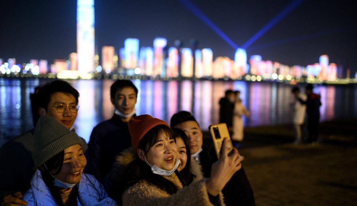 Orang-orang menurunkan masker wajah mereka untuk mengambil selfie sebelum hitung mundur Tahun Baru di Wuhan di provinsi Hubei, China (31/12/2020). Jalanan penuh sesak dan perayaan Tahun Baru ramai di kota Wuhan di China sementara seluruh dunia mengalami penguncian. (AFP/Noel Celis)