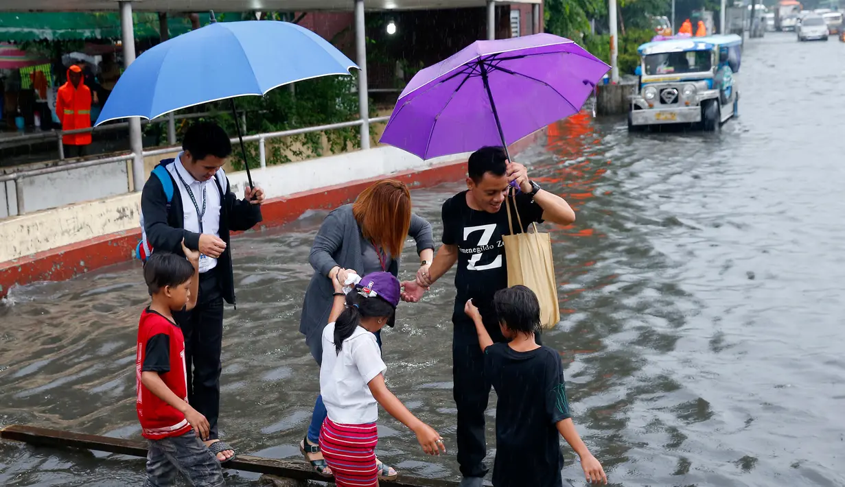 Sejumlah anak-anak membantu warga menyebrangi genangan air di Manila, Filipina, Kamis (27/7). PAGASA mengatakan bahwa hembusan angin saat badai terjadi dengan kecepatan maksimum 85 kilometer per jam (53 mil per jam). (AP/Bullit Marquez)