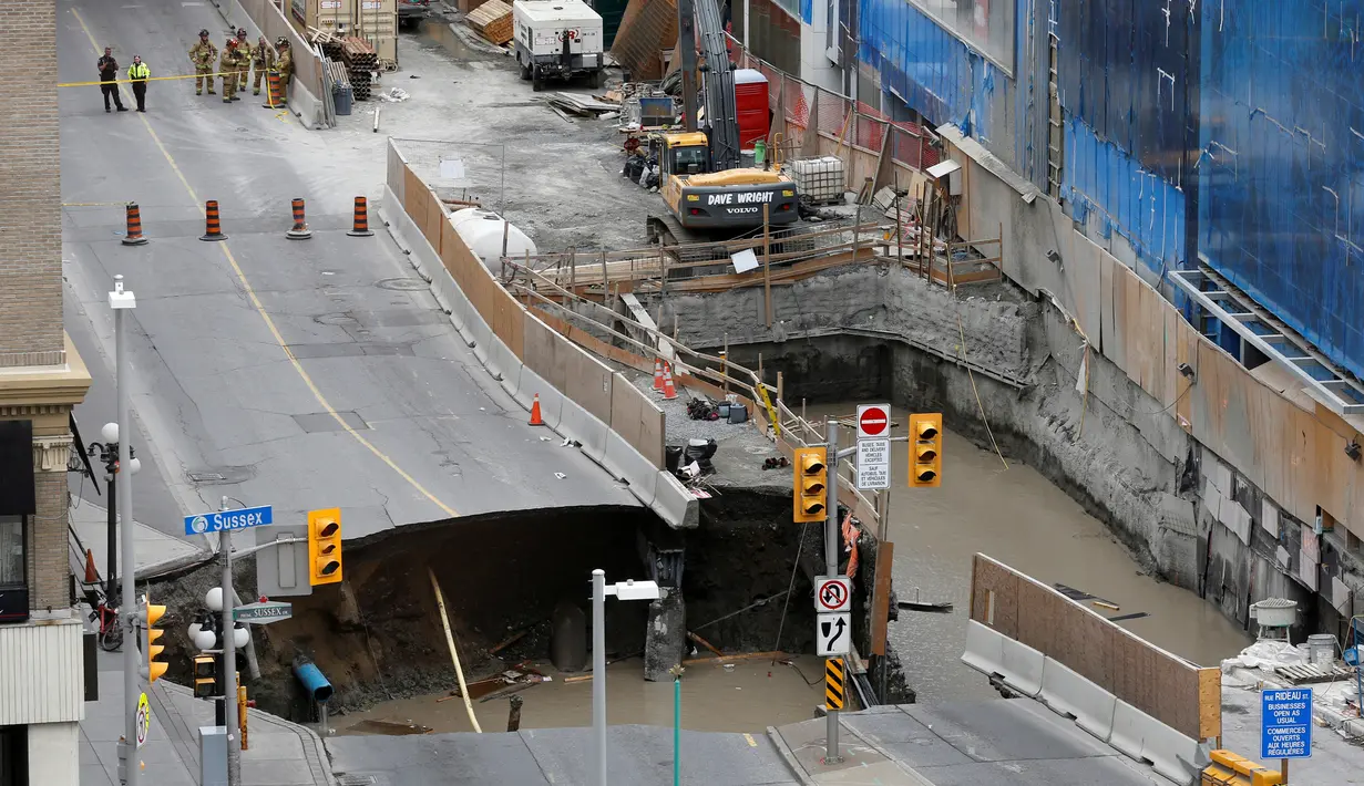 Petugas keselamatan darurat melihat sinkhole besar di Rideau Street, Ottawa, Kanada, Rabu (8/6). Awalnya sebuah lubang berdiameter 5 meter dilaporkan menganga, lalu sinkhole makin membesar hingga mencakup seluruh jalur dan trotoar. (REUTERS/Chris Wattie)