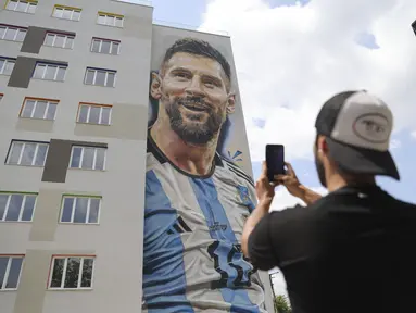 Seniman jalanan Argentina Maximiliano Bagnasco mengambil foto mural yang menggambarkan superstar sepak bola Argentina Lionel Messi, yang ia lukis, di Tirana, Albania, pada Kamis (8/6/2023). (AP Photo/Llazar Semini)