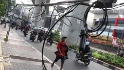 Pejalan kaki melintasi trotoar yang terhalang instalasi kabel di Jalan Kyai Maja, Jakarta, Rabu (10/4). Selain menganggu kenyamanan pejalan kaki, kondisi instalasi kabel yang semrawut tersebut juga berbahaya apabila mengandung aliran listrik. (Liputan6.com/Immanuel Antonius)