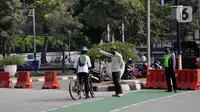 Petugas gabungan mengarahkan pengguna sepeda saat pengalihan jalur pesepeda di kawasan Sudirman-Thamrin, Jakarta, Minggu (5/9/2021). Pemberlakuan jalur ganjil genap pada masa PPKM membuat pengguna sepeda dilarang melintasi kawasan ganjil-genap pagi ini. (Liputan6.com/Angga Yuniar)