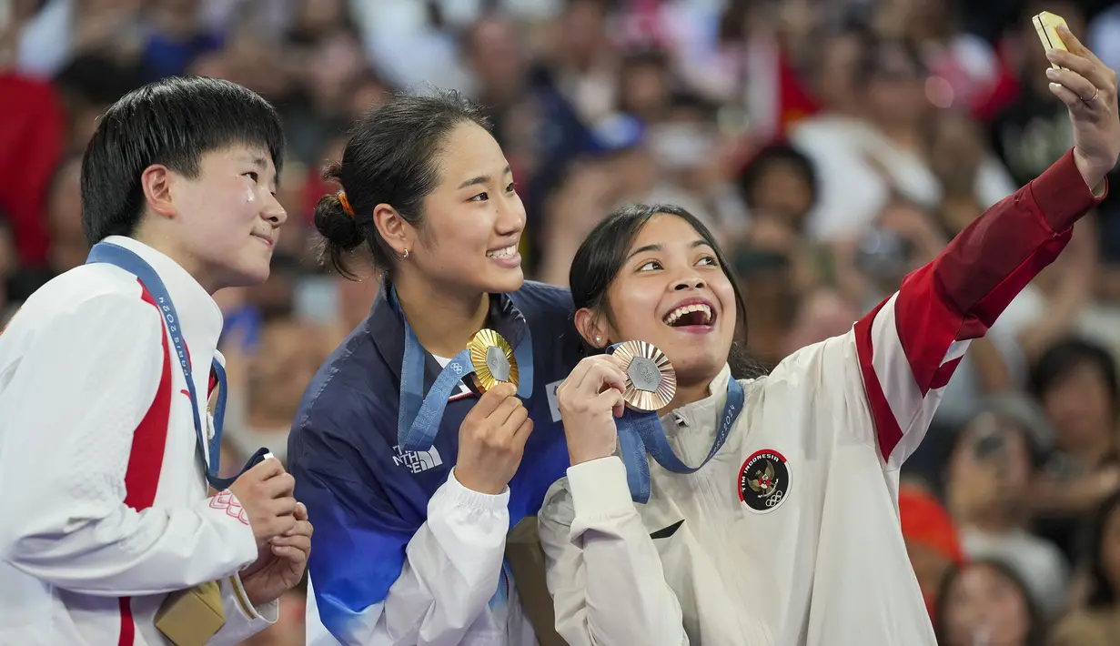 Pebulu tangkis tunggal putri Indonesia, Gregoria Mariska Tunjung sukses menyumbang medali pertama bagi kontingen Indonesia di Olimpiade Paris 2024. Medali perunggu yang didapatnya tanpa harus bertanding menghadapi Carolina Marin yang mundur akibat cedera di semifinal, dirayakan Jorji di atas podium juara dengan berswafoto dengan peraih medali emas, An Se-young dan peraih medali perak, He Bing Jiao saat upacara penyerahan medali di Porte de La Chapelle Arena, Paris, Senin (5/8/2024). (AP Photo/Kin Cheung)