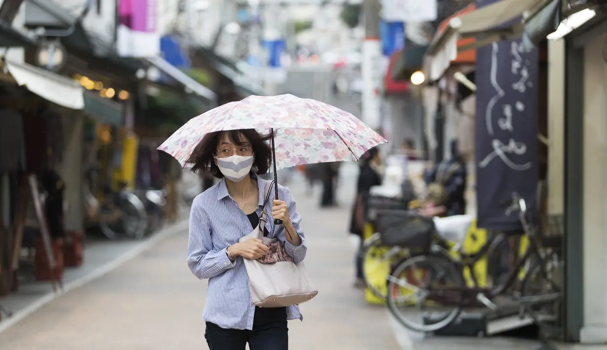 Seorang wanita dengan masker wajah berjalan melalui jalan perbelanjaan di tengah hujan di Tokyo (15/10/2020). Ibukota Jepang mengonfirmasi lebih dari 280 kasus virus korona baru pada hari Kamis. (AP Photo/Hiro Komae)