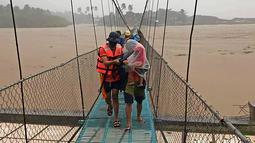 Tim penyelamat membantu warga menyeberangi jembatan saat dievakuasi di kota Tubay, Agusan del Norte, Filipina selatan, Kamis (16/12/2021). Puluhan ribu orang sedang dievakuasi ke tempat yang aman ketika Topan Rai mendekati pada Kamis (16/12). (Philippine Coast Guard via AP)