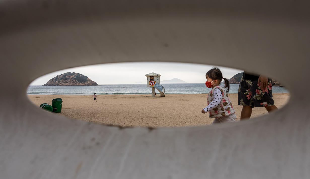 Orang-orang berjalan ketika pekerja memasang pagar untuk memblokir akses ke Pantai Shek O di Hong Kong, Kamis (17/3/2022). Pemerintah Hong Kong mengatakan akan menutup pantai umum untuk mengekang penyebaran virus corona COVID-19. (DALE DE LA REY/AFP)