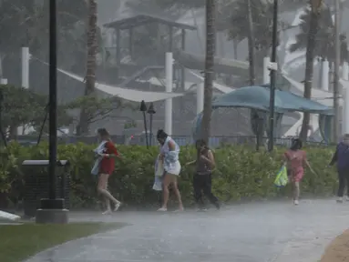 Warga berebut keluar dari guyuran hujan deras di Pantai Waikiki, Honolulu (6/12/2021). Badai kuat yang membawa angin kencang dan hujan yang sangat deras membanjiri jalan-jalan dan meruntuhkan kabel listrik dan cabang-cabang pohon di seluruh Hawaii. (AP Photo/Caleb Jones)