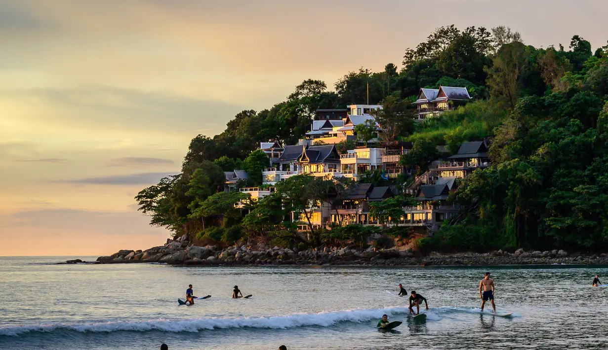 Orang-orang berselancar di pantai, saat para turis memanfaatkan program "Kotak Pasir Phuket" untuk pengunjung yang telah divaksinasi penuh terhadap virus corona Covid-19 di pulau Phuket Thailand (25/10/2021). (AFP/Mladen Antonov)