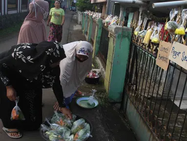 Warga menggantungkan sayuran, beras, dan bumbu masak untuk digantungkan pada pagar rumah di Gang Palautan, Cilodong, Depok, Jumat (21/1/2022). Warga Rt 04 Rw 01 di kawasan tersebut secara swadaya berbagi setiap hari Jumat kepada warga lainnya yang terdampak pandemi. (Liputan6.com/Herman Zakharia)