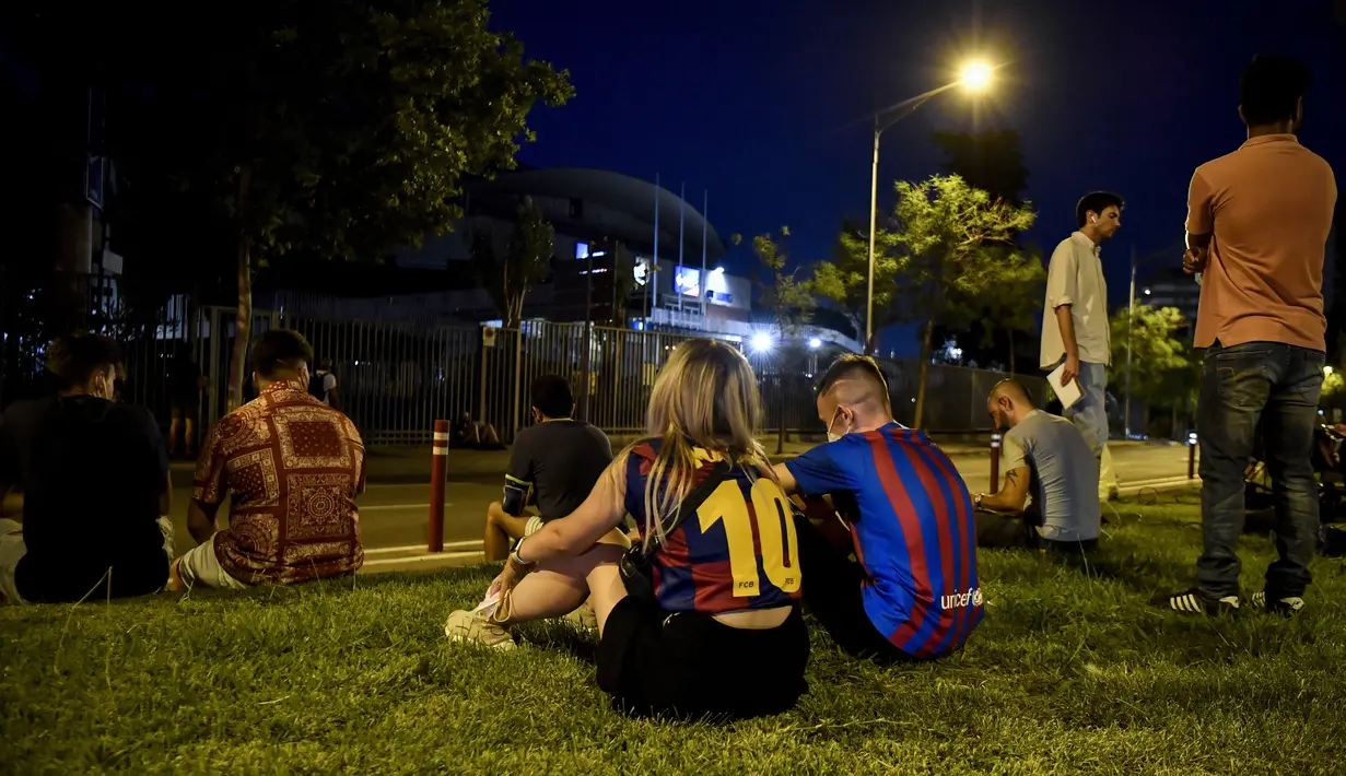 Para fans duduk saat berkumpul di luar stadion Camp Nou di Barcelona (5/8/2021). Messi yang melakukan debut di Barcelona pada 2004, telah memenangkan 10 gelar La Liga dan empat Liga Champions. (AFP/Pau Barrena)
