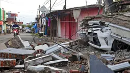 Pengendara sepeda motor melewati mobil yang terkubur puing reruntuhan bangunan akibat gempa di Mamuju, Sulawesi Barat, Indonesia, Senin (18/1/2021). Sebanyak 253 warga mengalami luka berat akibat gempa di Kabupaten Majene dan Mamuju. (AP Photo/Yusuf Wahil)