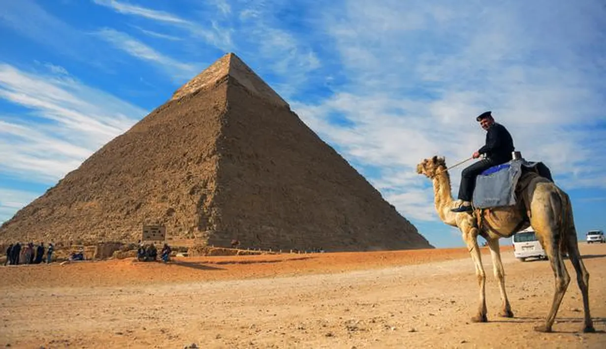 Seorang pria menunggang unta dengan latar belakang piramida Khafre yang berada di dataran tinggi Giza di pinggiran barat daya ibukota Kairo, Mesir (6/12). (AFP Photo/Mohamed El-Shahed)