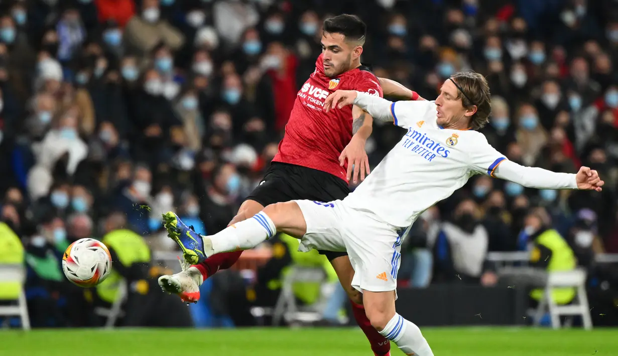 Bek Valencia Hugo Guillamon (kiri) berebut bola dengan gelandang Real Madrid Luka Modric pada laga pekan ke-20 La Liga Spanyol di Santiago Bernabeu Valencia, Minggu dini hari WIB (9/1/2022). Real Madrid menang meyakinkan 4-1 atas Valencia. (GABRIEL BOUYS / AFP)
