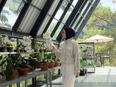 Irish Bella berada di sebuah rumah kaca yang penuh dengan tanaman anggrek. Ia terlihat menikmati keindahan bunga-bunga tersebut, mengenakan pakaian bernuansa krem yang elegan. Lokasi ini memberikan kesan tenang dan asri, memperkuat suasana romantis yang mungkin sedang mereka rasakan selama bulan madu. (Liputan6.com/IG/@_irishbella_)