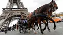 Sejumlah orang mengendarai kereta kuda melintas di depan Menara Eiffel saat mengikuti parade kuda ke-20 di Paris, Prancis (19/11). (AFP Photo/Thomas Samson)