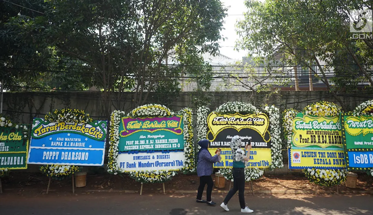 Pelayat mengambil gambar karangan bunga yang menghiasi jalan menuju rumah duka Presiden ke-3 RI BJ Habibie di Kuningan, Jakarta, Kamis (12/9/2019). Ucapan belasungkawa terus mengalir melalui karangan bunga dari berbagai elemen masyarakat. (Liputan6.com/Immanuel Antonius)