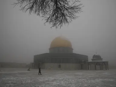 Seorang pria berjalan di dekat the Dome of the Rock atau Kubah Batu di kompleks Masjid Al Aqsa pada pagi bersalju di Kota Tua Yerusalem (18/2/2021). Salju yang mulai turun pada Rabu (17/2) malam juga menyelimuti kompleks Masjid Al-Aqsa. (AP Photo/Mahmoud Illean)
