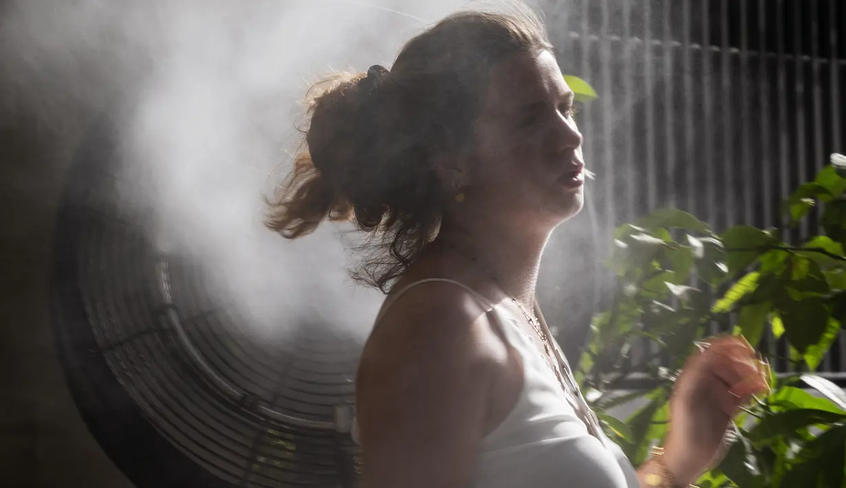 Seorang perempuan mendinginkan tubuh di depan kipas yang menyemprotkan uap air selama gelombang panas di Madrid, Spanyol, Sabtu (14/8/2021). Spanyol mengalami hari terpanas sepanjang tahun pada hari Sabtu dengan suhu mencapai 46 derajat Celcius. (AP Photo/Andrea Comas)