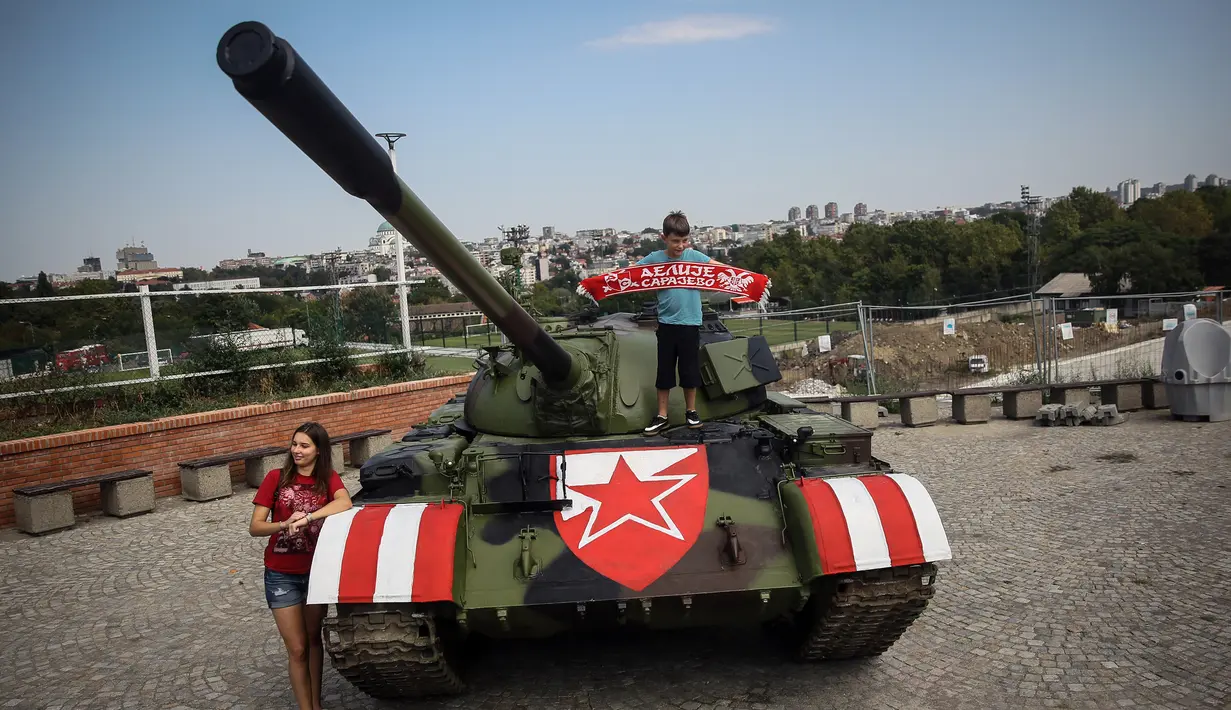 Suporter Red Star Belgrade berpose di tank T-55 yang terparkir di tribun utara Stadion Rajko Mitic, Belgrade, Serbia, Selasa (27/8/2019). Kehadiran tank tersebut memicu protes dari pihak Kroasia yang sempat berperang merebut kemerdekaannya dari Yugoslavia. (OLIVER BUNIC/AFP)