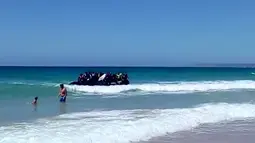 Seorang pria dan anak laki-laki menyaksikan  perahu karet yang dipenuhi imigran mendekati tepi pantai Cadiz di Spanyol selatan, 9 Agustus 2017. Puluhan imigran tersebut langsung melompat ke air dan berlarian menuju pantai. (Carlos Sanz via AP)