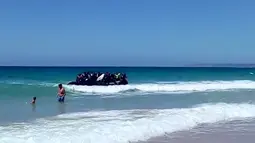 Seorang pria dan anak laki-laki menyaksikan  perahu karet yang dipenuhi imigran mendekati tepi pantai Cadiz di Spanyol selatan, 9 Agustus 2017. Puluhan imigran tersebut langsung melompat ke air dan berlarian menuju pantai. (Carlos Sanz via AP)