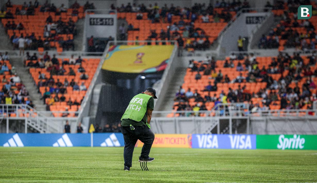 Petugas mengecek rumput setelah air yang menggenangi lapangan Jakarta International Stadium (JIS) akibat hujan deras jelang laga perempat final Piala Dunia U-17 2023 antara Timnas Brasil U-17 melawan Timnas Argentina U-17, Jumat (24/11/2023). (Bola.com/Bagaskara Lazuardi)