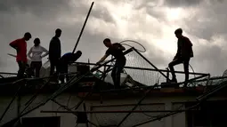 Sejumlah warga membersihkan puing-puing di sebuah bangunan setelah badai tornado menghantam Regla, Kuba (28/1). Hantaman tornado juga merobohkan tiang-tiang listrik di daerah tersebut. (AP Photo/Ramon Espinosa)